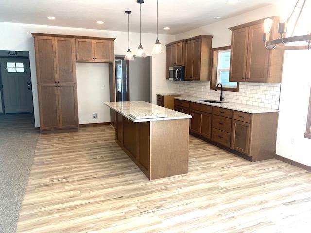 kitchen featuring light stone counters, stainless steel appliances, sink, a center island, and hanging light fixtures