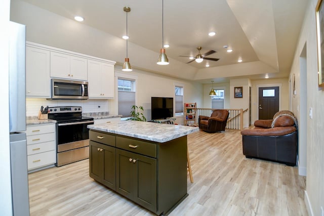 kitchen with pendant lighting, a center island, white cabinets, appliances with stainless steel finishes, and a tray ceiling