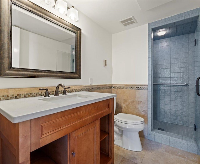 bathroom with tile patterned floors, vanity, tile walls, toilet, and a shower with shower door