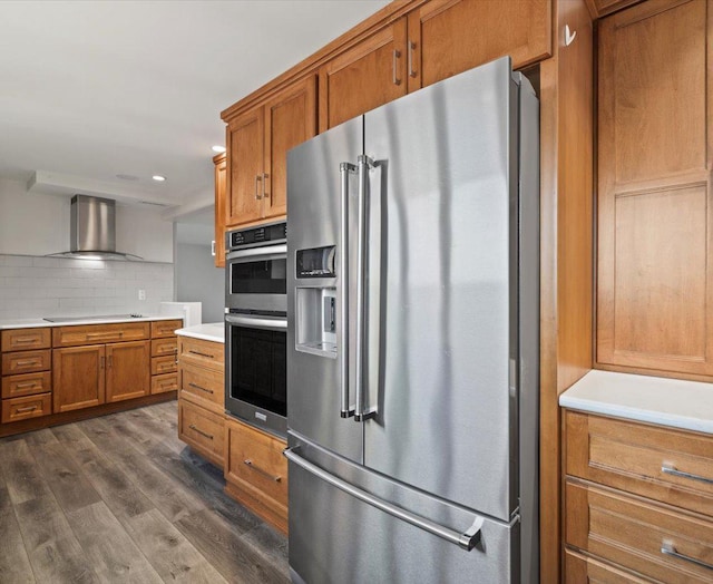 kitchen featuring dark wood-type flooring, stainless steel appliances, tasteful backsplash, and wall chimney exhaust hood