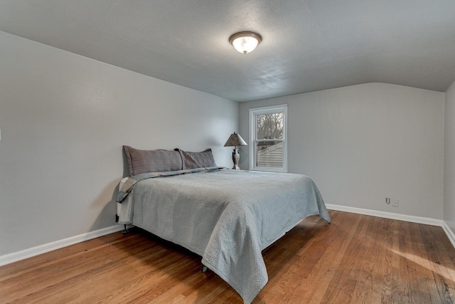 bedroom with a textured ceiling, hardwood / wood-style flooring, and vaulted ceiling