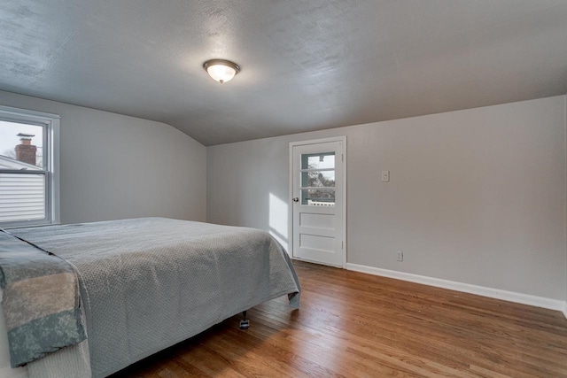 bedroom with a textured ceiling, hardwood / wood-style flooring, vaulted ceiling, and multiple windows