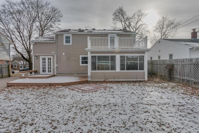 snow covered house with a sunroom, a balcony, french doors, and a deck