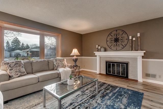 living room featuring wood-type flooring, a textured ceiling, and a brick fireplace