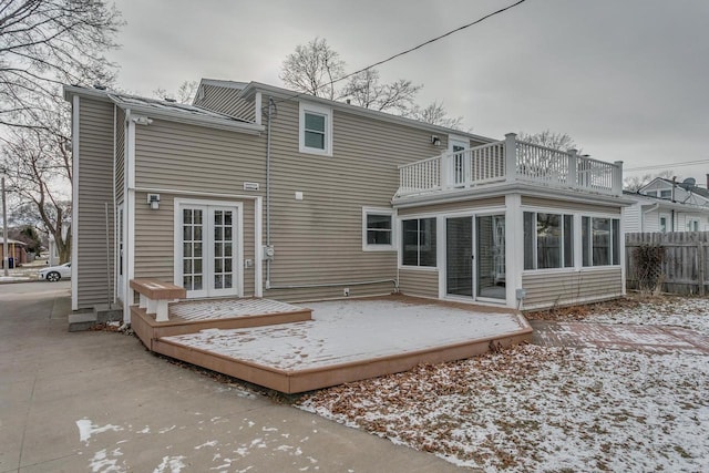 snow covered rear of property featuring a sunroom, a balcony, a wooden deck, and french doors