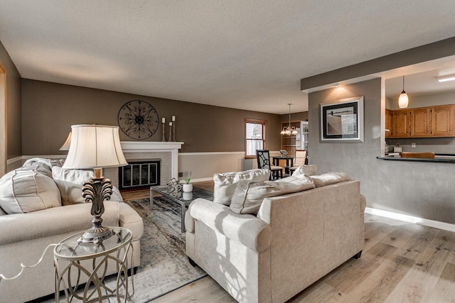 living room with a notable chandelier, light wood-type flooring, a textured ceiling, and a brick fireplace