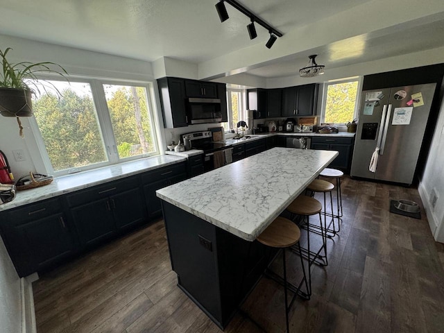 kitchen with light stone countertops, dark hardwood / wood-style floors, a breakfast bar, a kitchen island, and appliances with stainless steel finishes