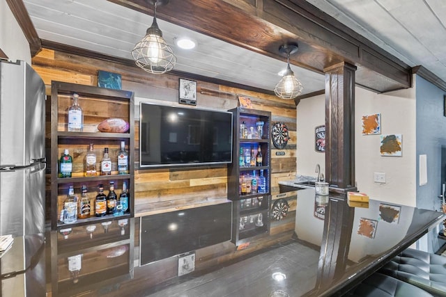 bar featuring sink, stainless steel refrigerator, crown molding, and wood walls