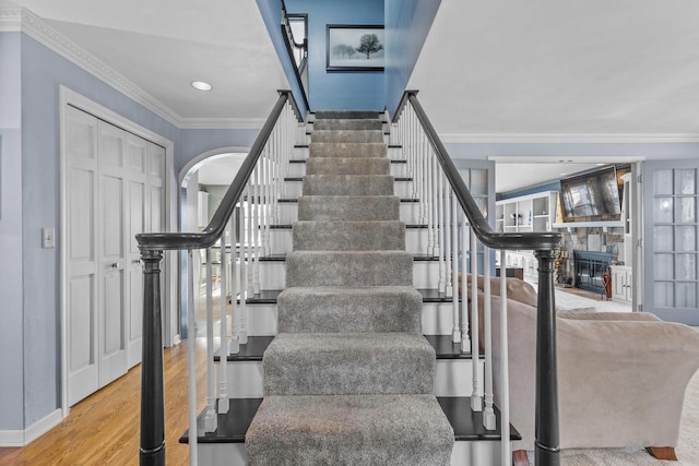 staircase featuring a fireplace, wood-type flooring, and ornamental molding