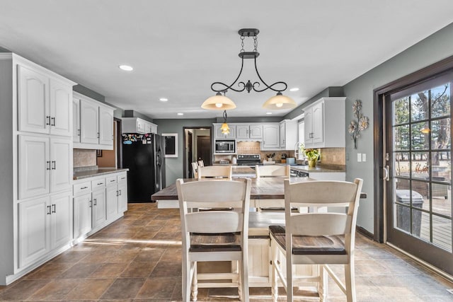 kitchen featuring a breakfast bar, stainless steel microwave, white cabinets, tasteful backsplash, and decorative light fixtures