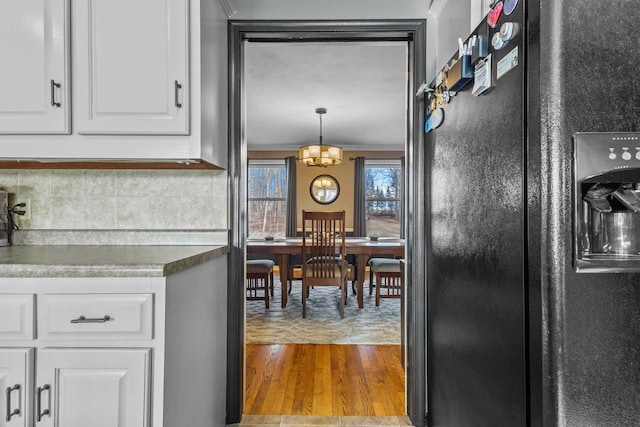 kitchen with pendant lighting, black refrigerator with ice dispenser, an inviting chandelier, hardwood / wood-style flooring, and white cabinetry