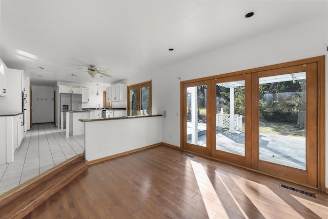 interior space featuring kitchen peninsula, stainless steel refrigerator with ice dispenser, light hardwood / wood-style flooring, ceiling fan, and white cabinetry