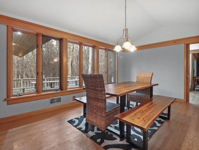 dining space with hardwood / wood-style floors, lofted ceiling, and an inviting chandelier