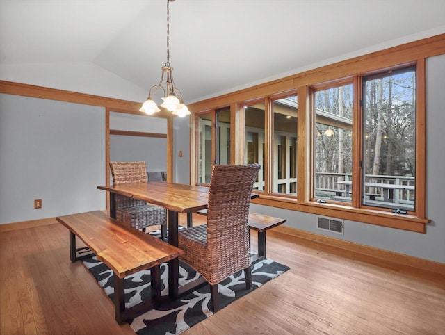 dining space with light wood-type flooring, vaulted ceiling, and a notable chandelier