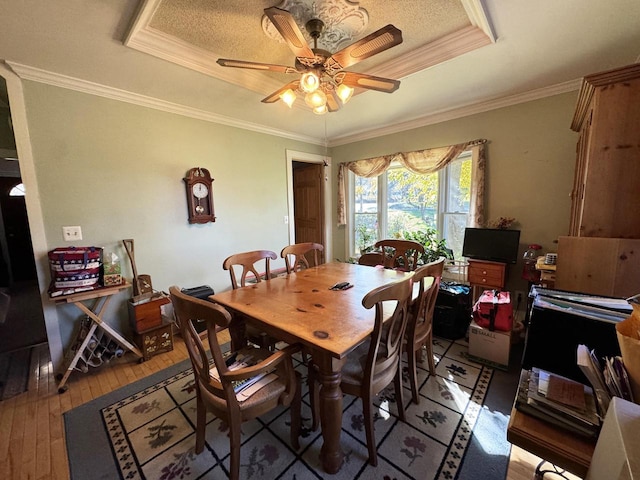 dining space with hardwood / wood-style floors, a raised ceiling, ceiling fan, and crown molding