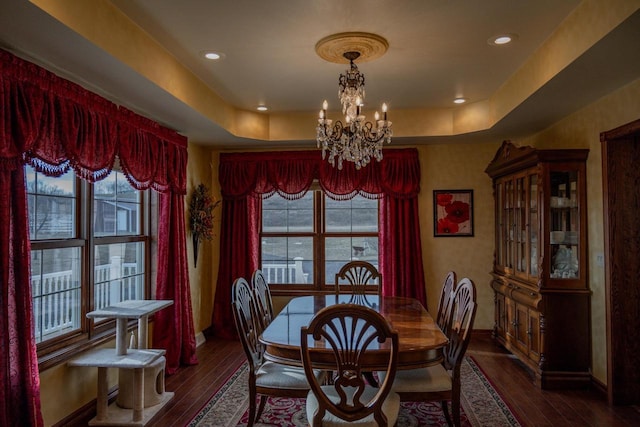 dining area with a tray ceiling, dark hardwood / wood-style flooring, and an inviting chandelier