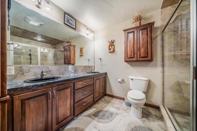 bathroom featuring vanity, toilet, a shower with door, and tasteful backsplash