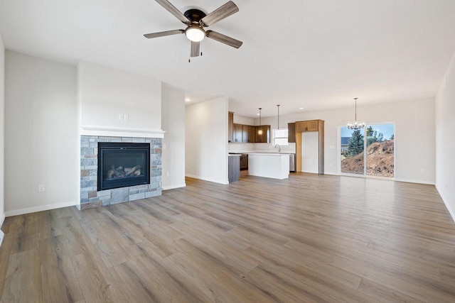 unfurnished living room with ceiling fan with notable chandelier, light wood-type flooring, and sink