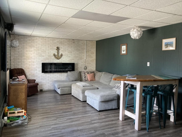 living room featuring hardwood / wood-style flooring, a drop ceiling, brick wall, and a brick fireplace