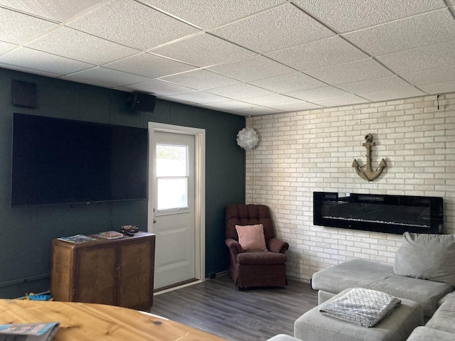 living room featuring hardwood / wood-style flooring, a paneled ceiling, and brick wall