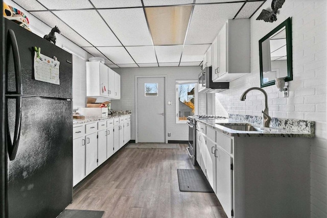 kitchen featuring black fridge, a drop ceiling, white cabinets, and sink