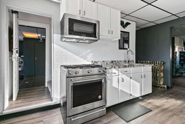 kitchen with a drop ceiling, sink, light stone countertops, appliances with stainless steel finishes, and white cabinetry