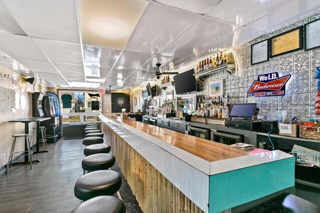 bar featuring ceiling fan, a drop ceiling, and wood-type flooring