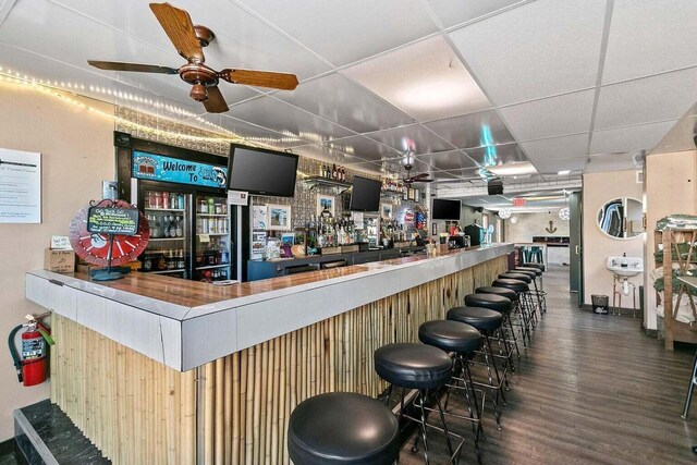 bar with a paneled ceiling, ceiling fan, and dark wood-type flooring