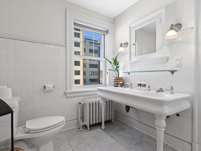 bathroom with toilet, radiator heating unit, tile walls, and tile patterned flooring