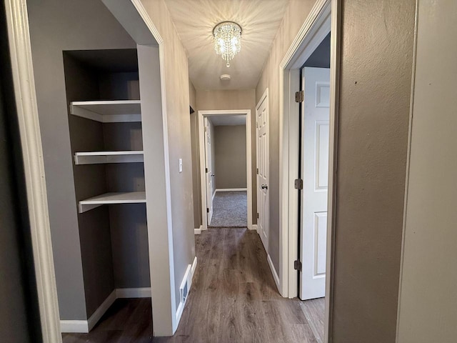 hallway featuring wood-type flooring, an inviting chandelier, and built in features