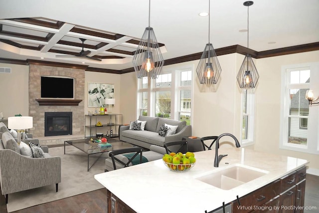 kitchen featuring a fireplace, a center island with sink, coffered ceiling, and sink