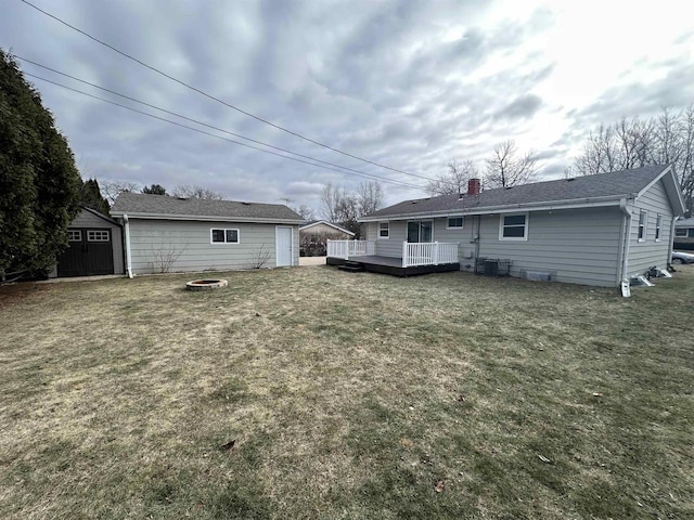 rear view of property with a storage unit, a deck, an outdoor fire pit, and a yard