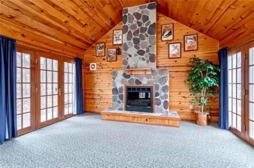 unfurnished living room featuring carpet flooring, french doors, a stone fireplace, and wood ceiling