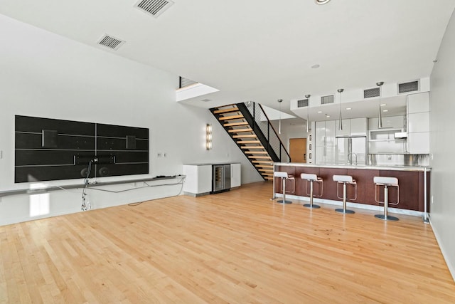 kitchen featuring a kitchen breakfast bar, light wood-type flooring, beverage cooler, sink, and decorative light fixtures