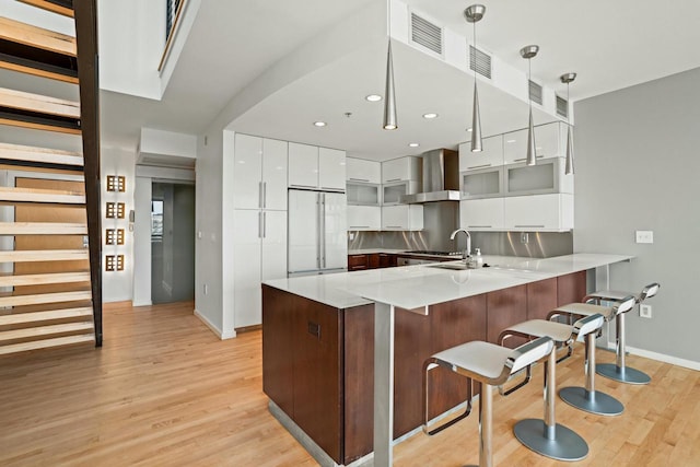 kitchen featuring kitchen peninsula, wall chimney exhaust hood, white fridge, white cabinetry, and hanging light fixtures