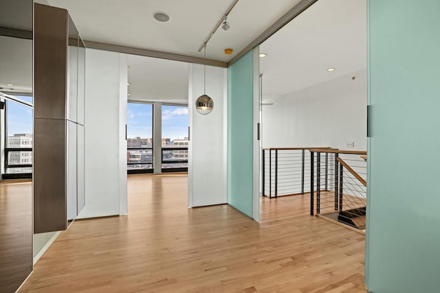 hall with light hardwood / wood-style floors, a wall of windows, and rail lighting