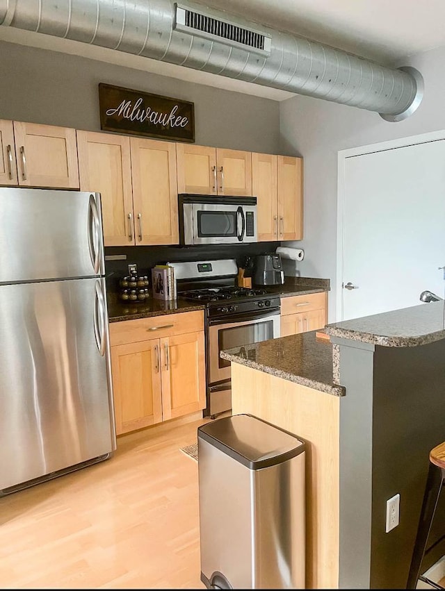 kitchen featuring a center island, light brown cabinets, appliances with stainless steel finishes, and dark stone counters