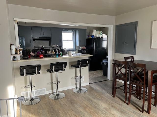 kitchen featuring a kitchen bar, kitchen peninsula, light wood-type flooring, and black fridge