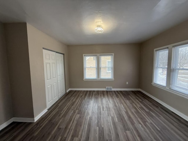 unfurnished bedroom featuring multiple windows, a closet, and dark wood-type flooring