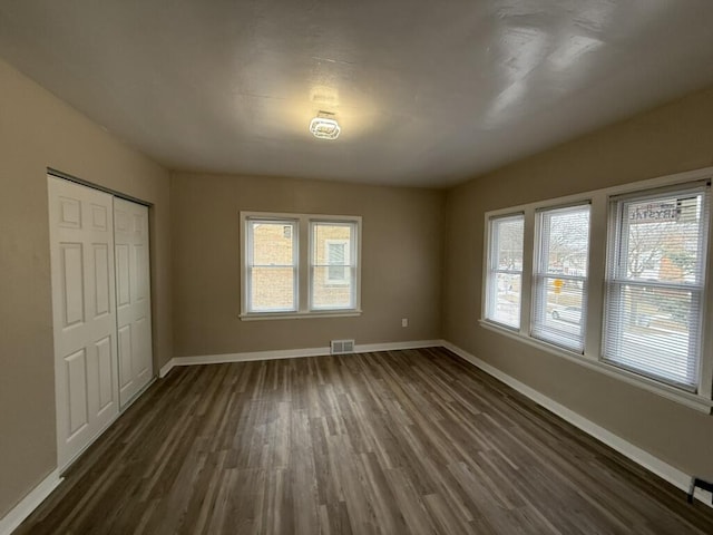 unfurnished bedroom featuring dark hardwood / wood-style flooring, a closet, and multiple windows