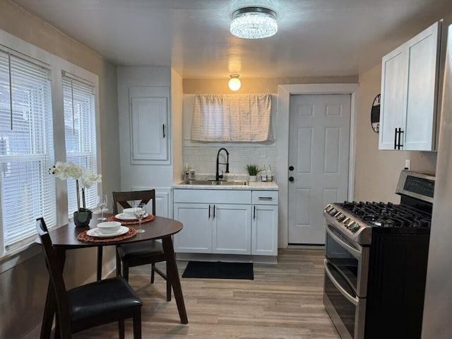 kitchen with stainless steel gas stove, white cabinetry, and sink