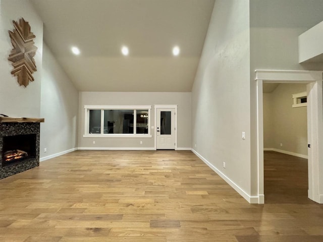 unfurnished living room featuring light hardwood / wood-style floors, a towering ceiling, and a tile fireplace