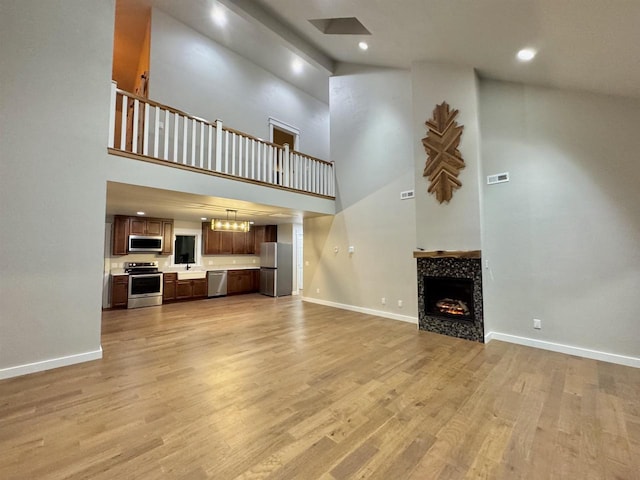 unfurnished living room with light hardwood / wood-style flooring, a high ceiling, and a tiled fireplace