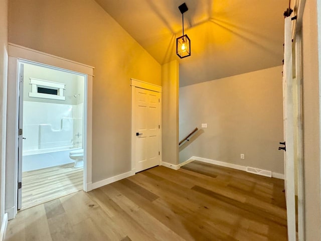 corridor with wood-type flooring and vaulted ceiling