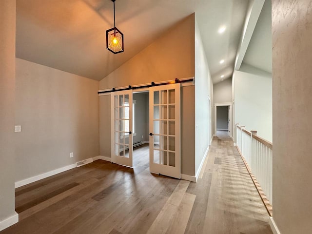 empty room featuring hardwood / wood-style flooring, a barn door, and high vaulted ceiling