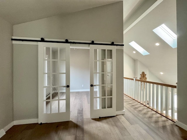 entryway with a barn door, vaulted ceiling with skylight, and light hardwood / wood-style floors