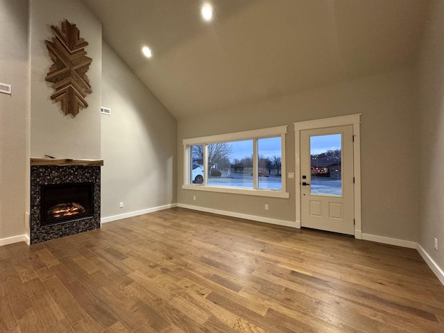 unfurnished living room featuring hardwood / wood-style floors, high vaulted ceiling, and a tile fireplace