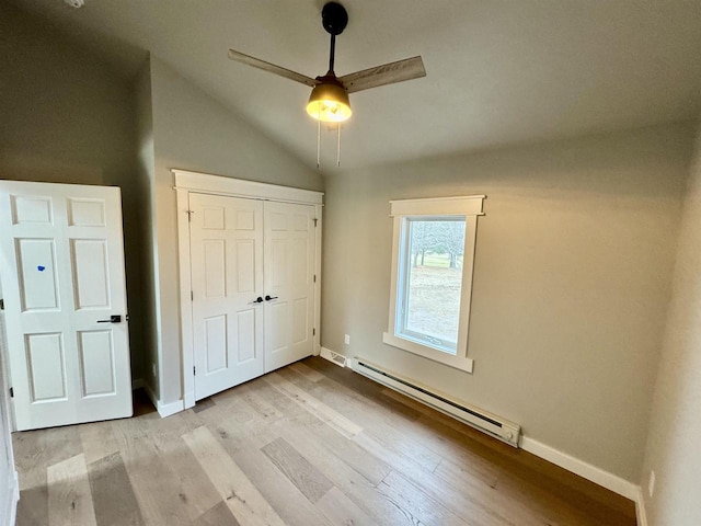 unfurnished bedroom featuring light hardwood / wood-style floors, lofted ceiling, baseboard heating, and a closet