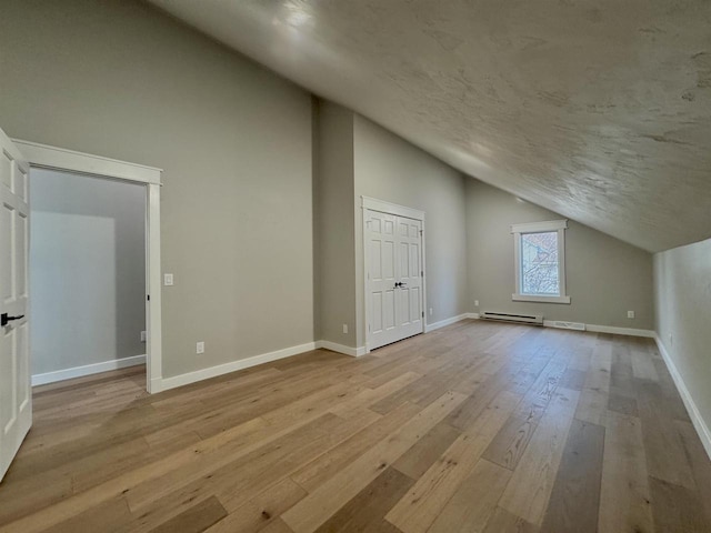 additional living space with light wood-type flooring, lofted ceiling, and a baseboard heating unit