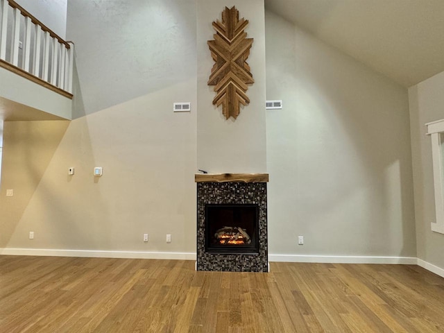 unfurnished living room with a fireplace, a towering ceiling, and hardwood / wood-style flooring